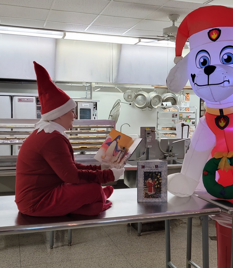 elf on the shelf in the cafeteria reading to a snow puppy